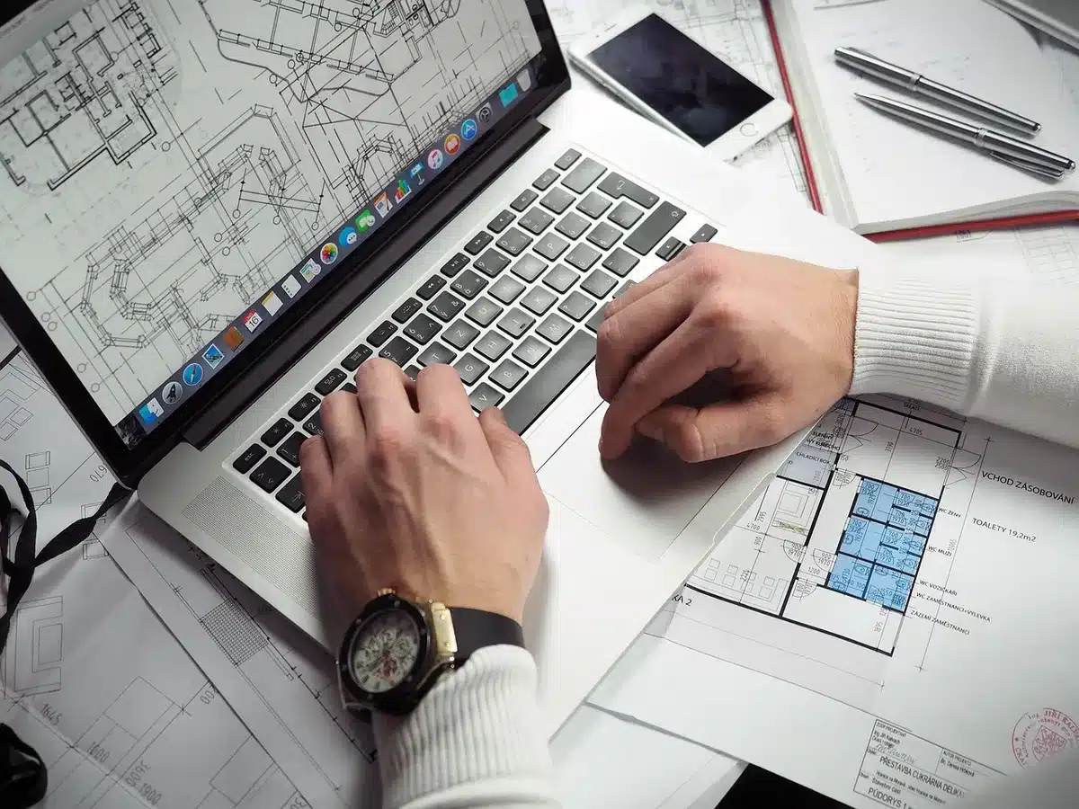 Mani anonime che digitano su un laptop con taccuino e caffè in uno spazio di coworking luminoso